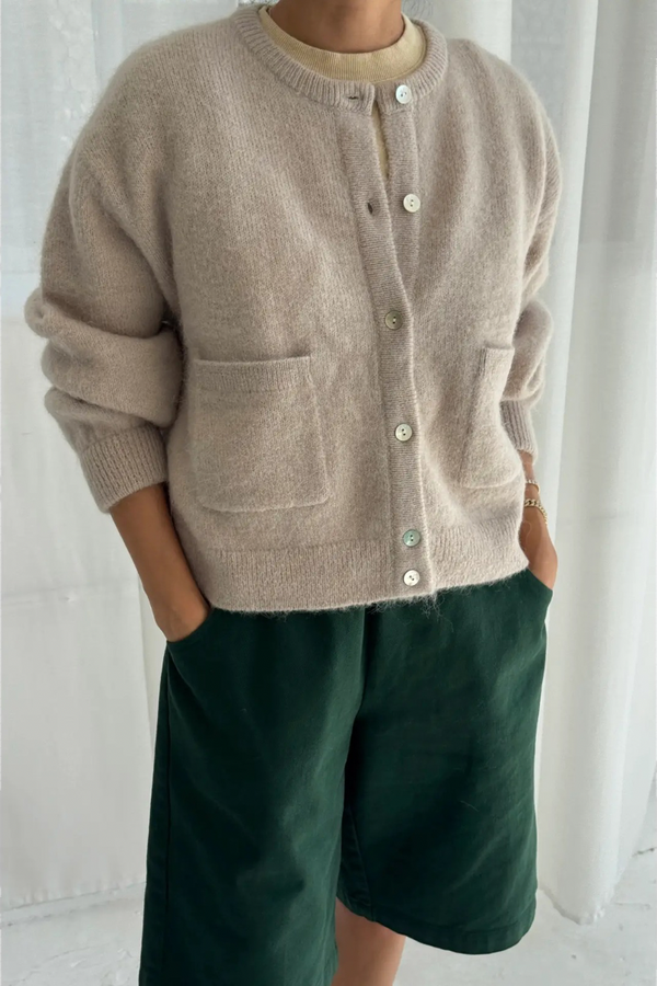 Person wearing a beige cardigan and green shorts against a white background