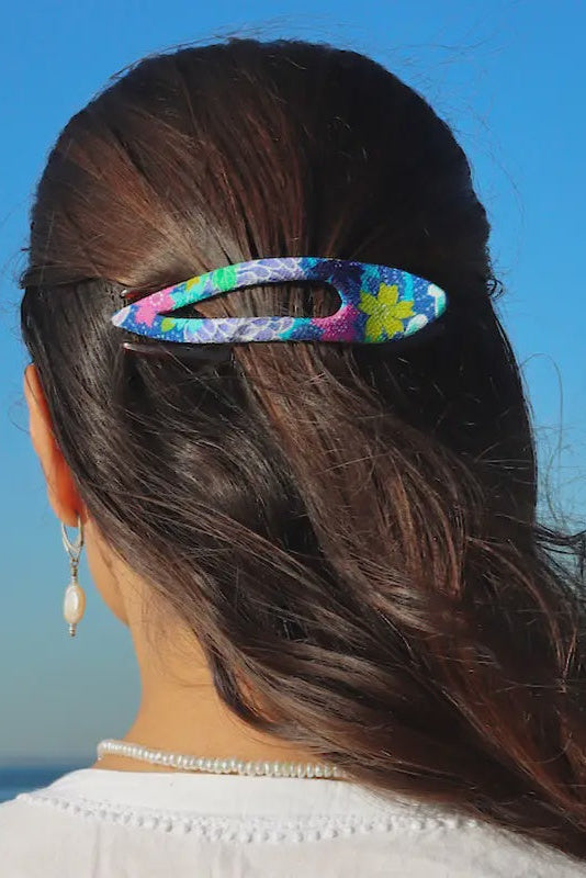 Person with a colorful floral hair clip against a blue sky