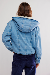 Person wearing a blue denim jacket with a hood on a plain background