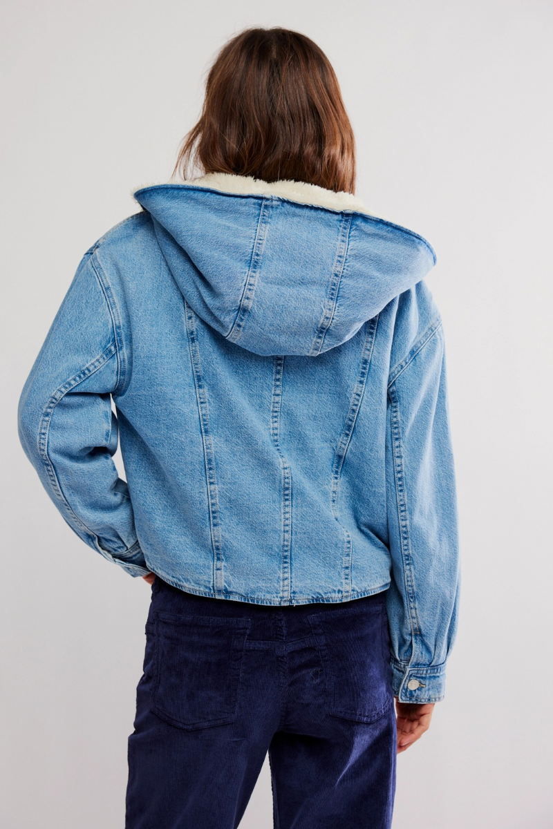Person wearing a blue denim jacket with a hood on a plain background