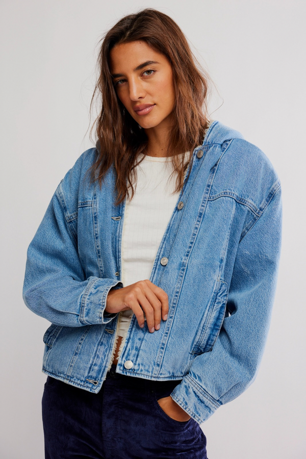 Woman wearing a blue denim jacket over a white shirt on a plain background