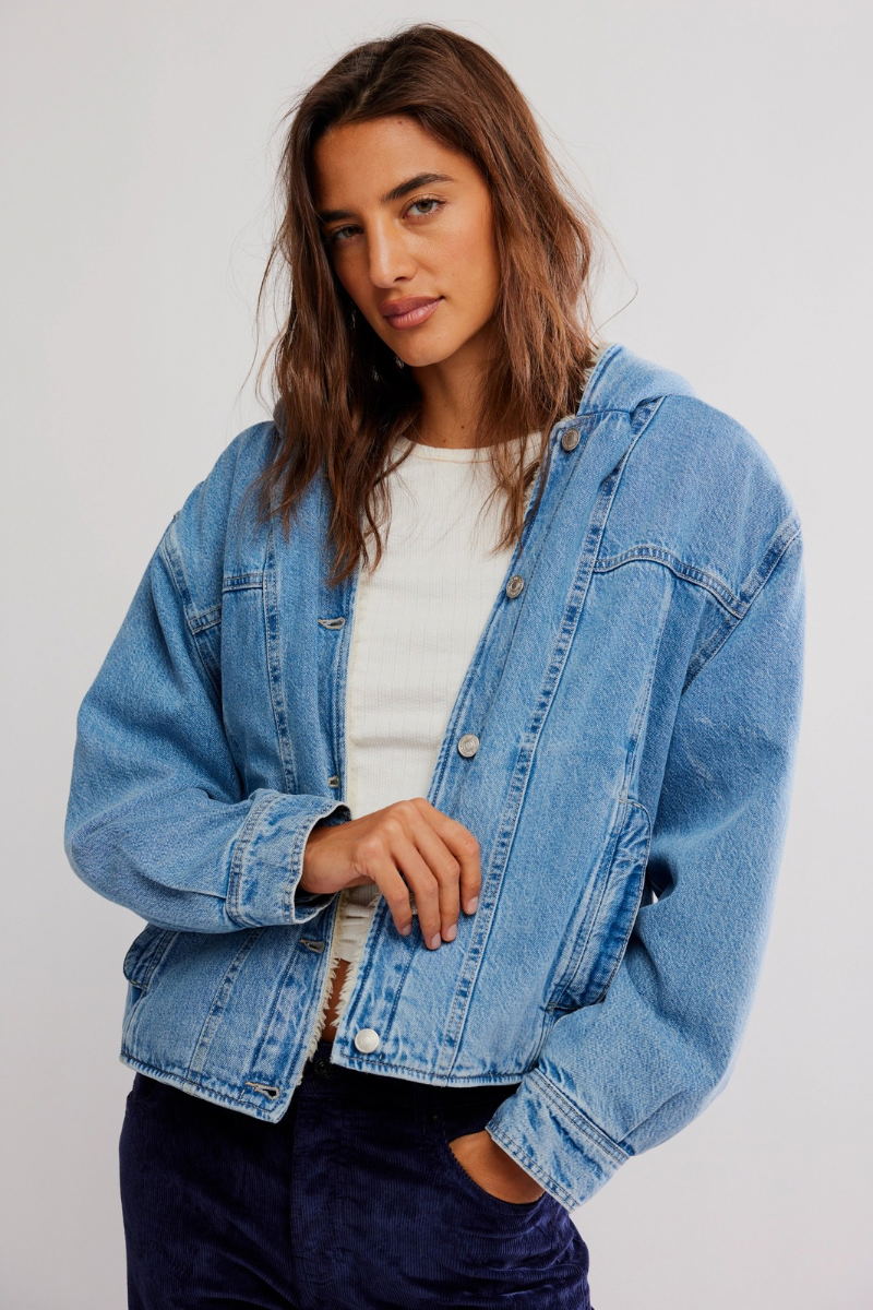 Woman wearing a blue denim jacket over a white shirt on a plain background