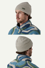 Man wearing a gray knit beanie with a brand logo, standing against a white background.