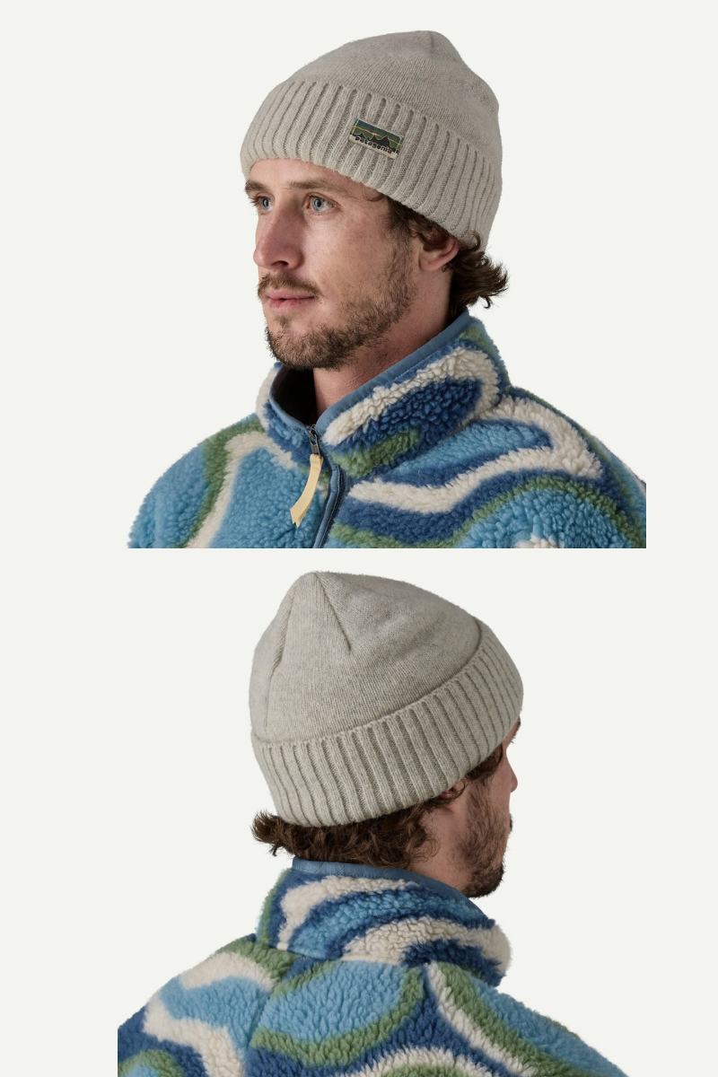 Man wearing a gray knit beanie with a brand logo, standing against a white background.