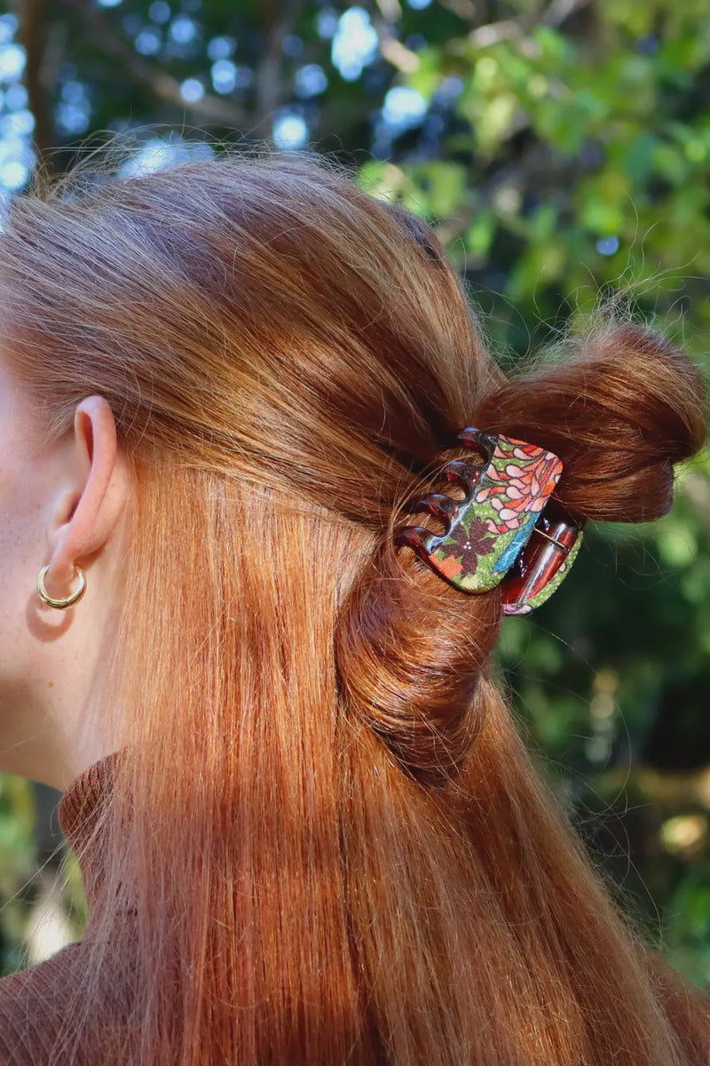 Person with red hair styled in a bun with a decorative hair clip, outdoors.