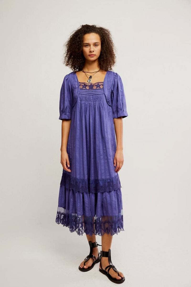 Woman wearing a purple dress with lace details on a plain background