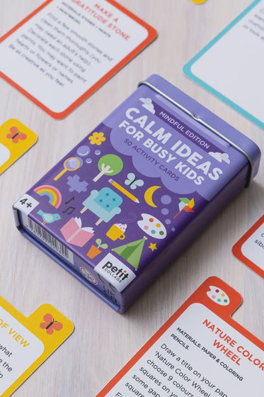 Purple card game box labeled 'Calm Ideas for Busy Kids' on a wooden surface with activity cards around it.