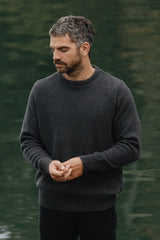 Man wearing a dark sweater standing by a body of water