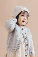 Child wearing a knitted cardigan and hat on a beige background