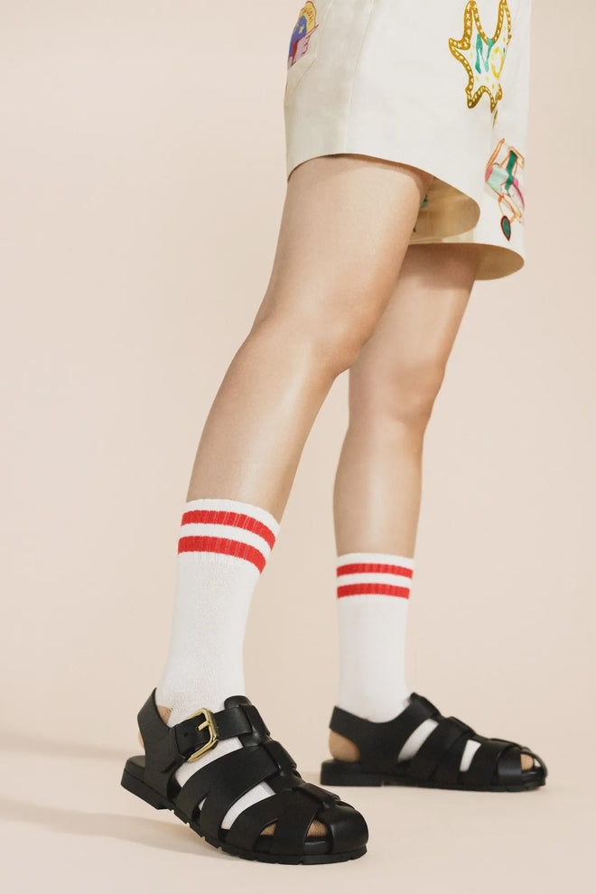 Person wearing black sandals and white socks with red stripes on a beige background