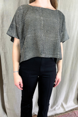 Person wearing a black and white striped top and black pants against a plain background