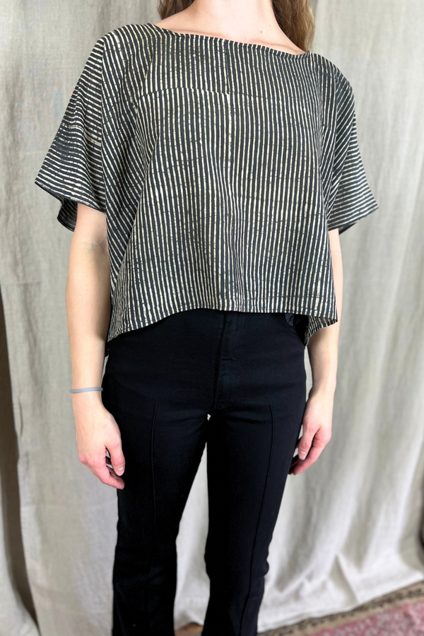 Person wearing a black and white striped top and black pants against a plain background