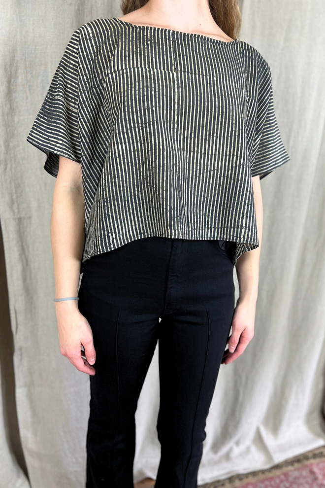 Person wearing a black and white striped top and black pants against a plain background
