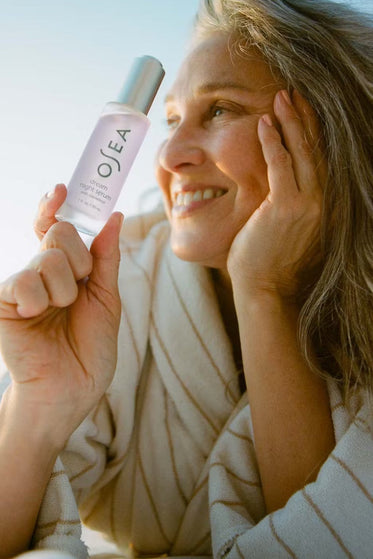 Woman holding a bottle of OSEA skincare product against a blurred natural background