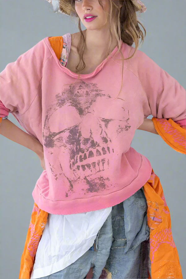 Person wearing a pink hoodie with a skull design, orange jacket, and gray pants on a white background