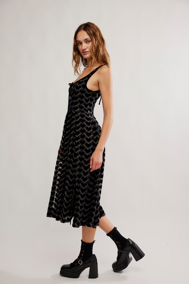 Woman wearing a black patterned dress with black boots on a white background
