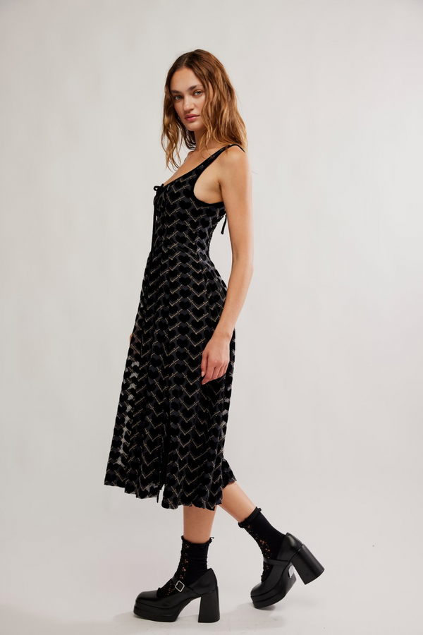 Woman wearing a black patterned dress with black boots on a white background