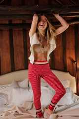Woman in red polka dot pants and white top standing on a bed with wooden paneling.