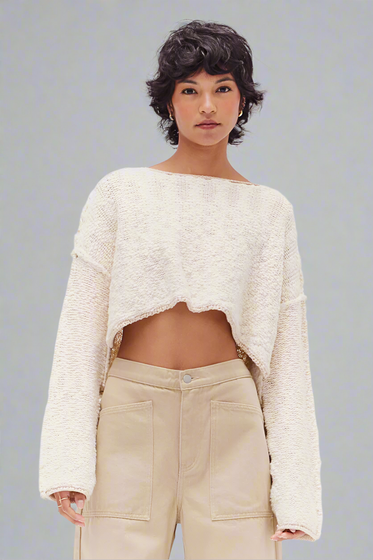A woman wearing a beige cotton slub crop top with long sleeves and a round neckline, paired with light beige trousers.