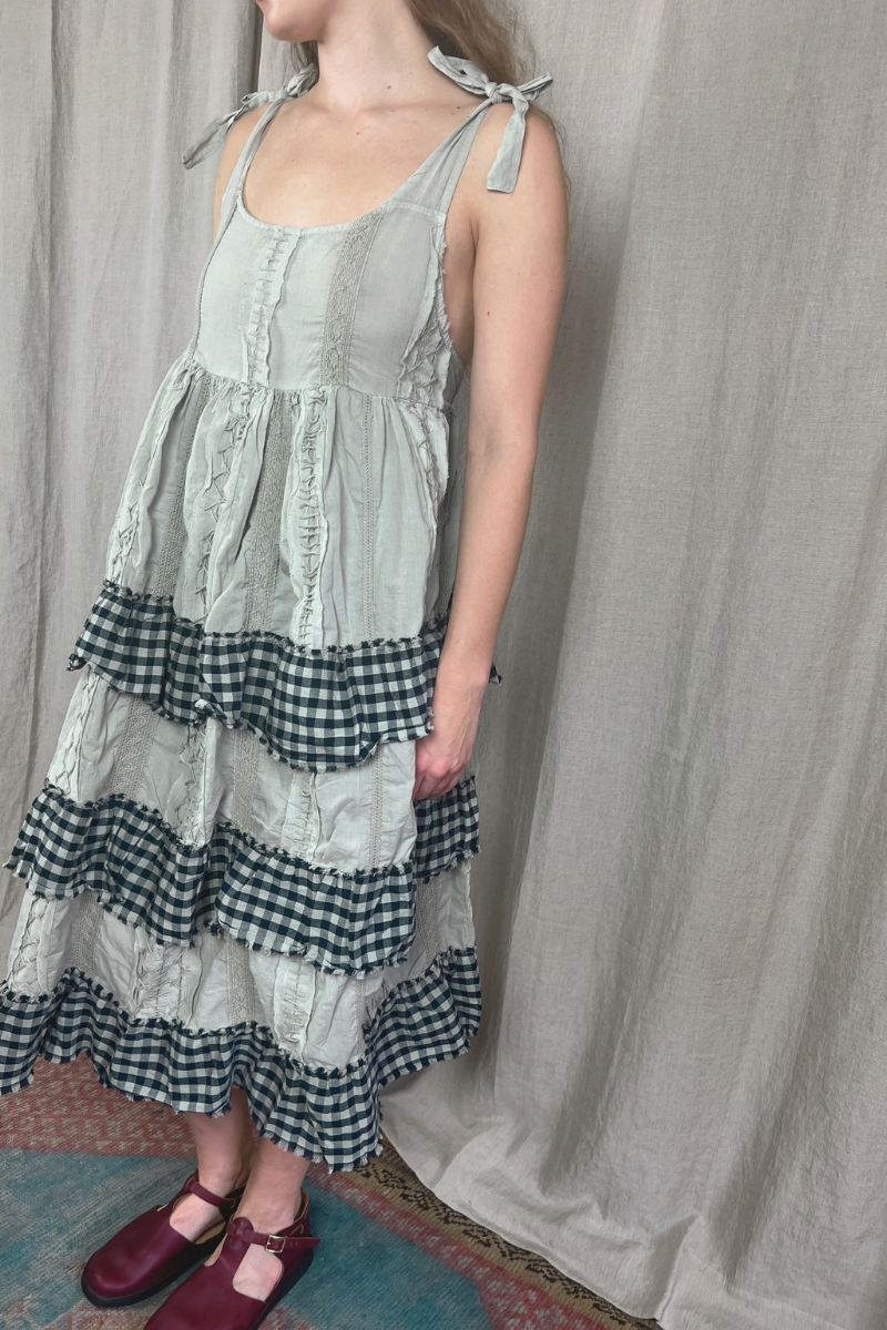 Person wearing a layered dress with green, black, and white patterns against a plain background