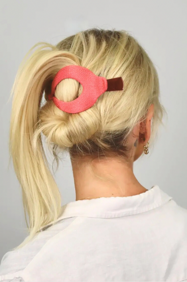 Person with blonde hair in a ponytail wearing a pink hair clip against a gray background