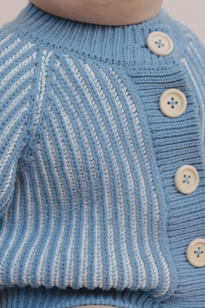 Close-up of a blue knitted sweater with buttons on a neutral background