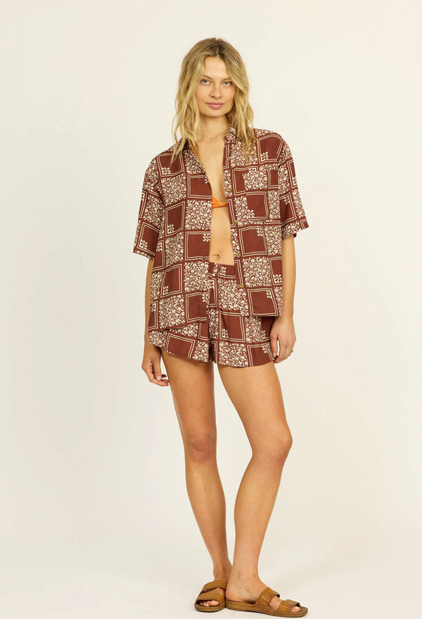 Woman wearing a matching brown and white patterned shirt and shorts set on a beige background