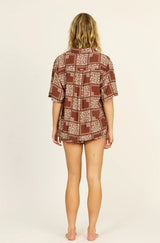 Woman wearing a patterned shirt and shorts on a beige background