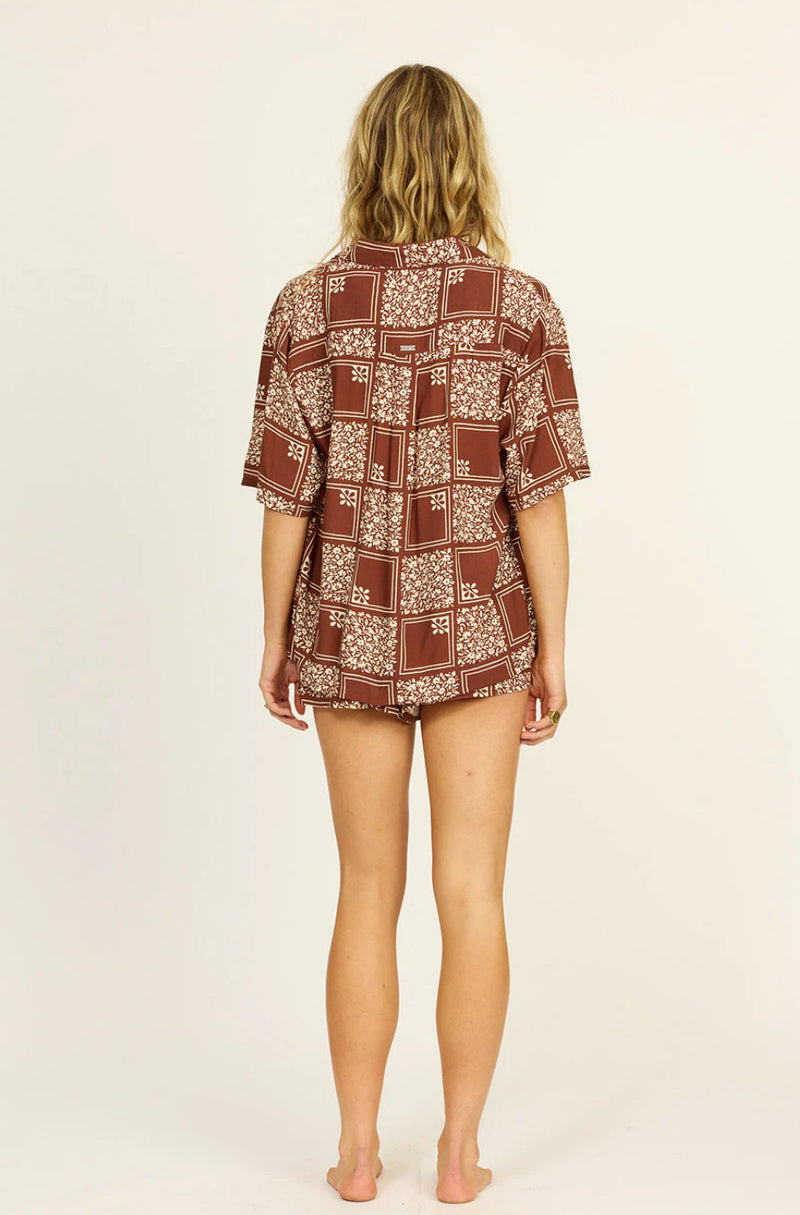 Woman wearing a patterned shirt and shorts on a beige background
