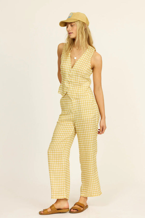 Woman wearing a yellow checkered two piece set and cap on a beige background