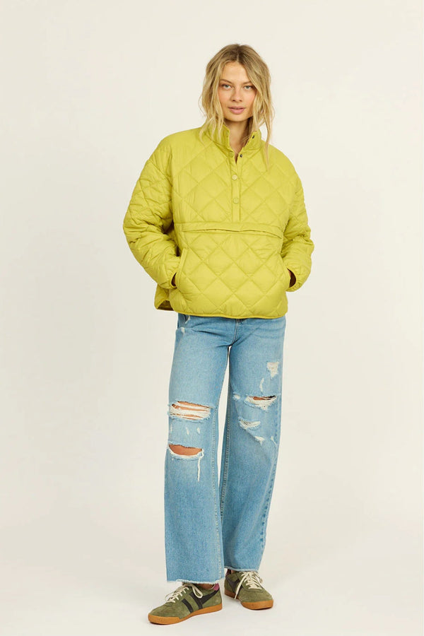 Person wearing a green quilted jacket and ripped jeans on a white background