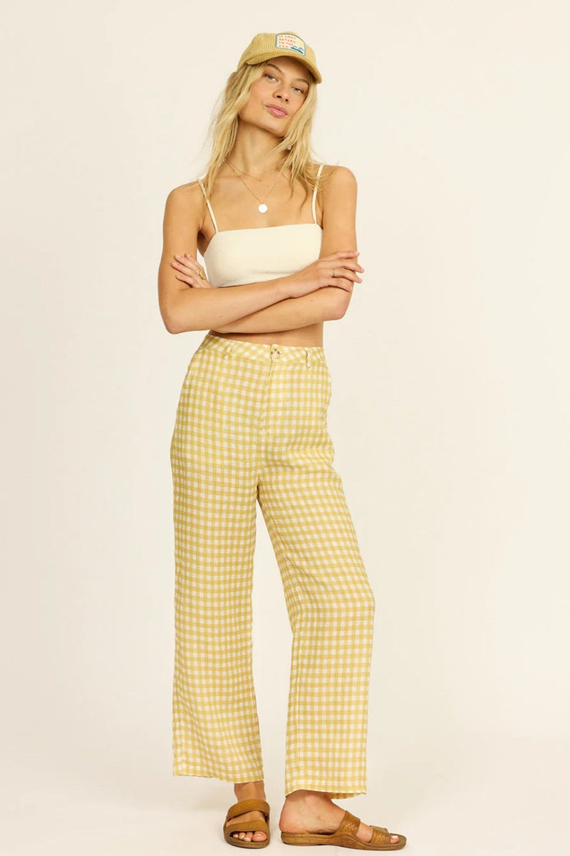 Woman wearing a white top and yellow checkered pants with a beige cap on a beige background
