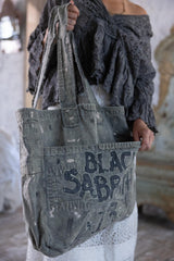 Person holding a distressed denim bag with 'Black Sabbath' branding.