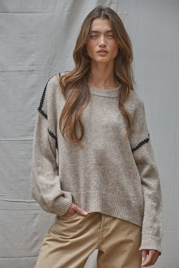 Woman wearing a beige sweater with black accents against a plain background