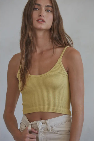 Woman wearing a yellow ribbed tank top against a plain background