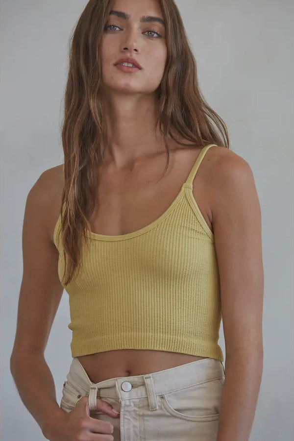 Woman wearing a yellow ribbed tank top against a plain background