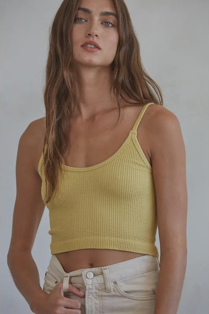 Woman wearing a yellow ribbed tank top against a plain background