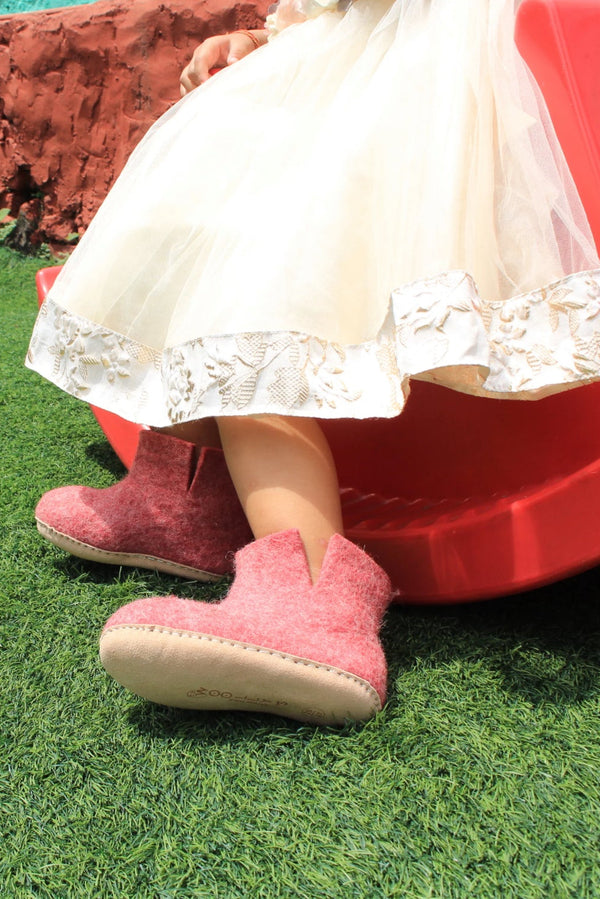 Child sliding down a red slide on grass with a white lace dress and pink shoes.