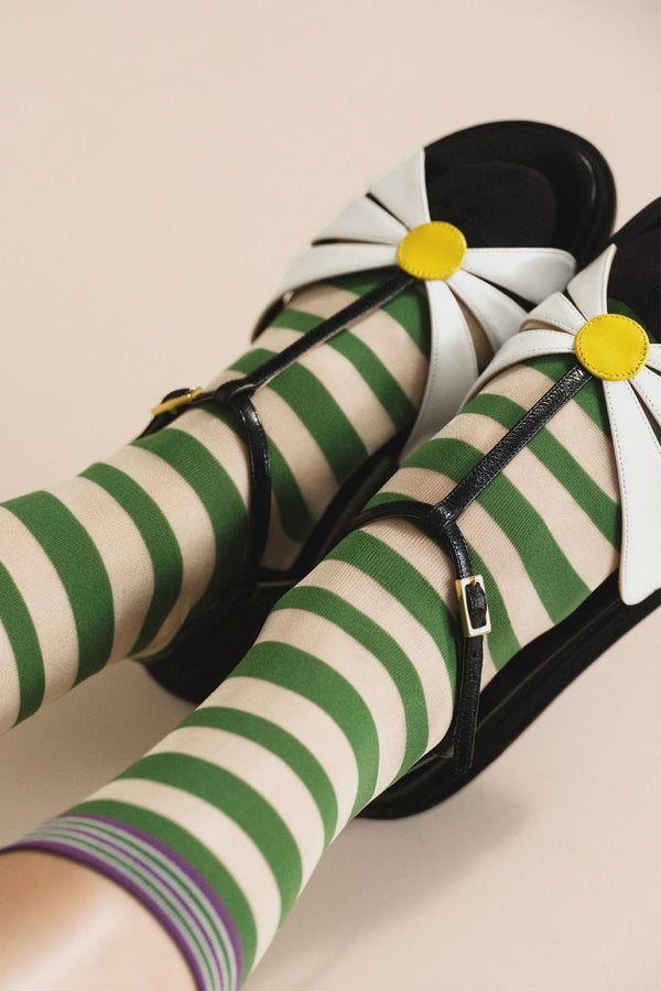 Green and white striped socks with black shoes and yellow flower details on a beige background