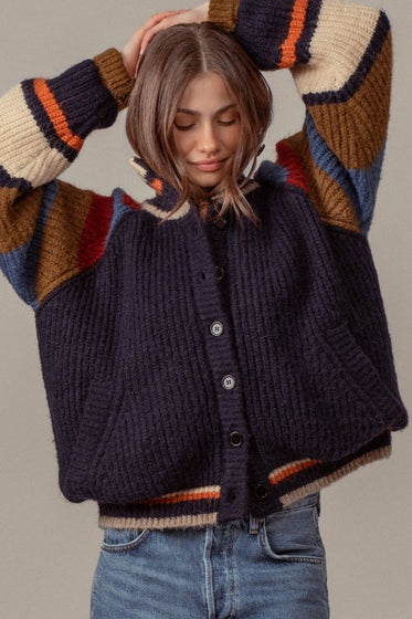 Woman wearing a dark blue knitted cardigan with colorful sleeves against a neutral background