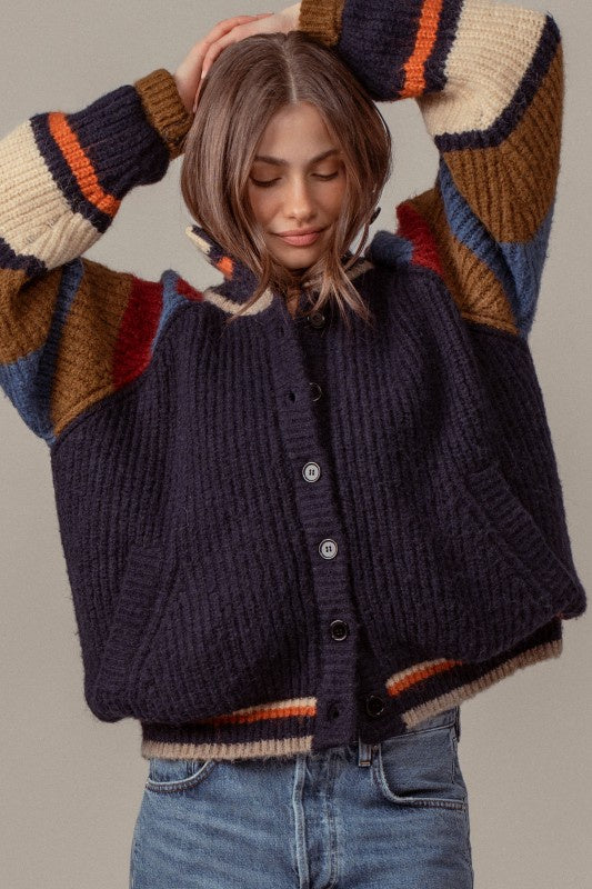Woman wearing a dark blue knitted cardigan with colorful sleeves against a neutral background
