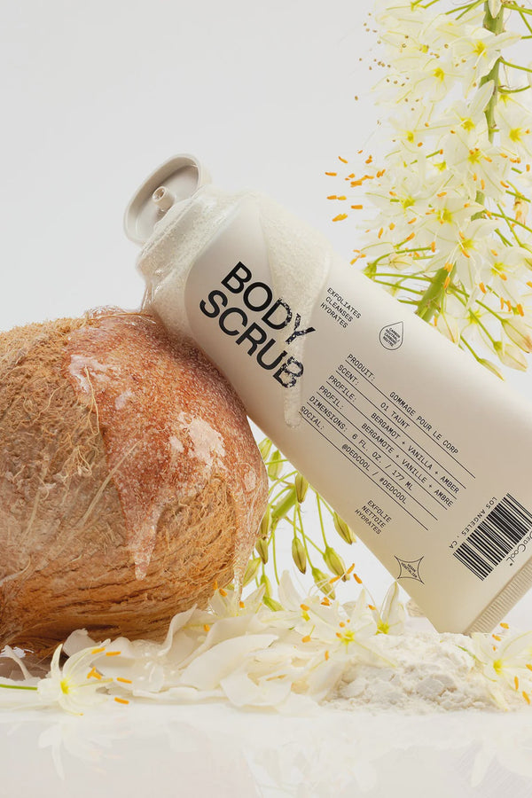Body scrub bottle with a coconut and flowers on a light background