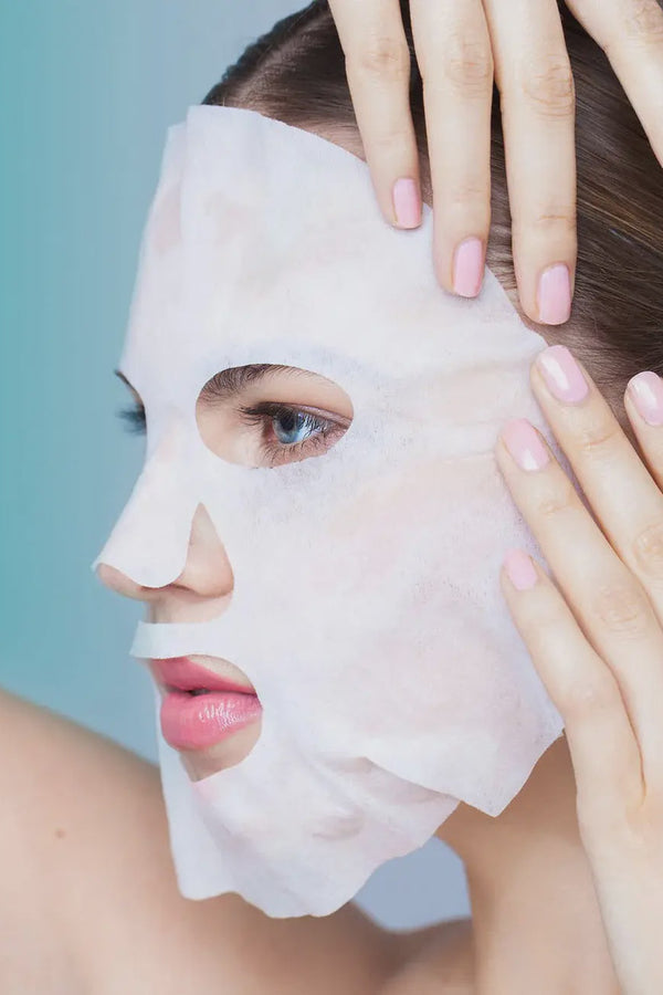 Woman applying a facial mask with hands on a light blue background