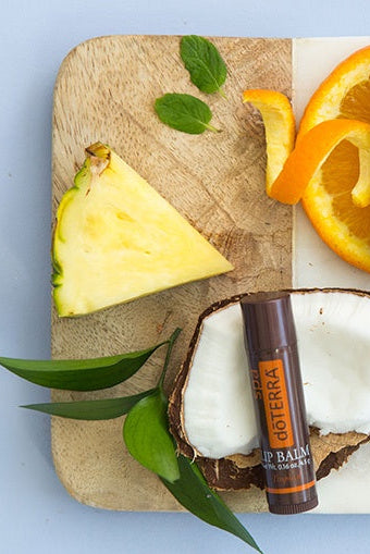 Lip balm tube on a cutting board with pineapple, coconut, and orange slices.