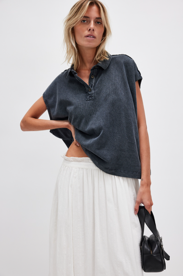 Woman wearing a dark denim shirt and white skirt with a black handbag on a white background
