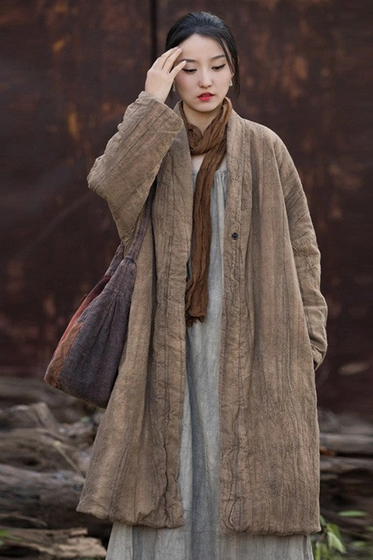 Woman wearing a long beige coat and brown scarf against a dark background