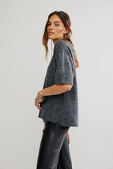 Woman wearing a gray sweater and dark pants on a light background