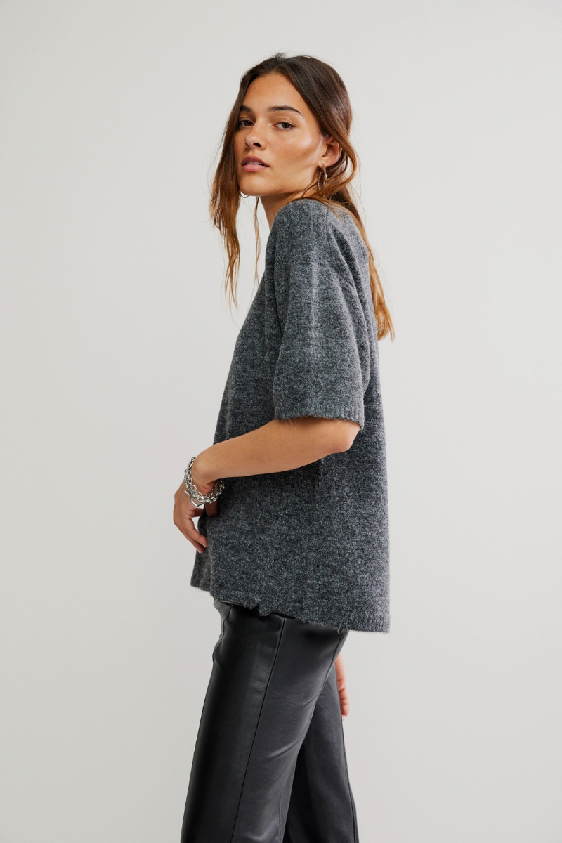Woman wearing a gray sweater and dark pants on a light background