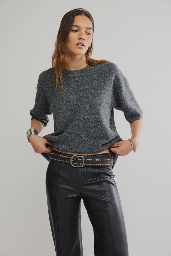 Woman wearing a gray sweater and black pants on a plain background