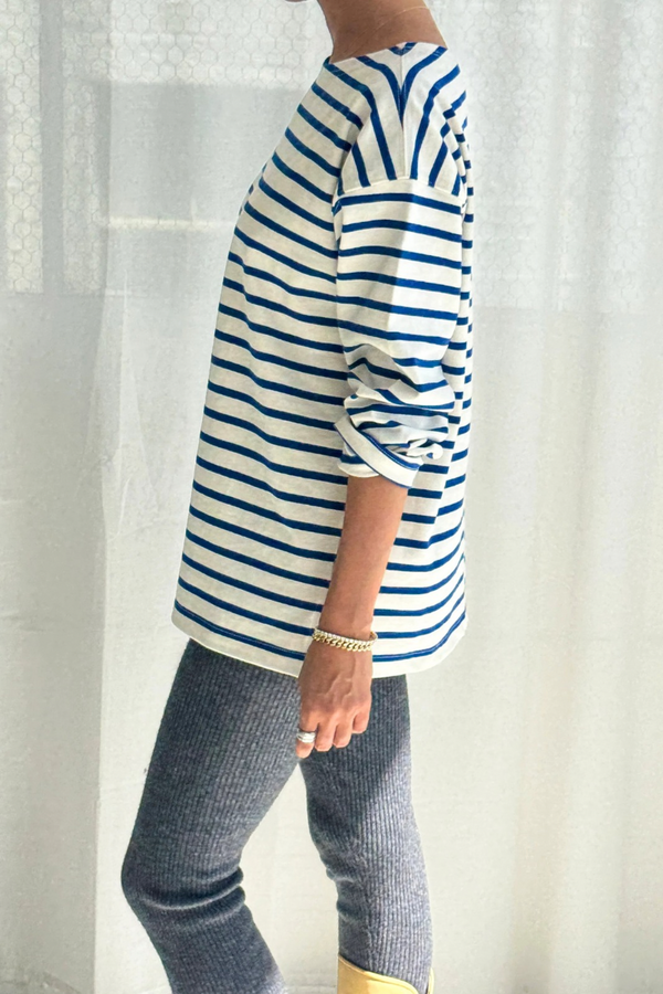 Person wearing a blue and white striped shirt with gray pants against a white curtain background